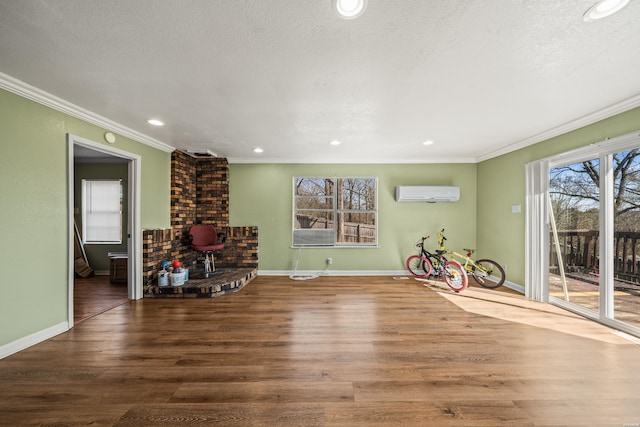 interior space featuring a textured ceiling, a wall unit AC, wood finished floors, baseboards, and ornamental molding