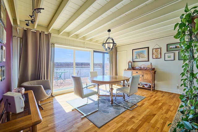 dining space featuring a water view, baseboards, light wood-type flooring, beamed ceiling, and track lighting