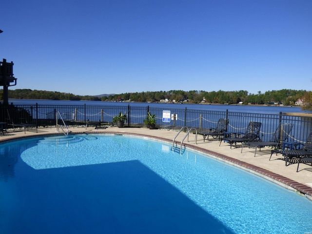 pool with a water view, fence, and a patio