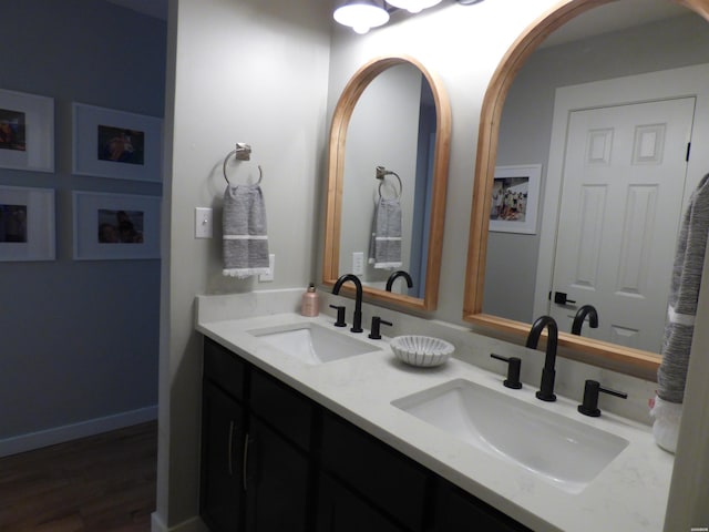 bathroom with wood finished floors, a sink, baseboards, and double vanity