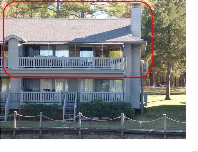 view of front of property with a balcony, a shingled roof, stairway, a chimney, and a front yard