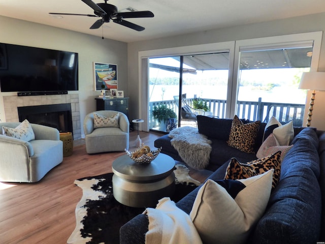 living room with a ceiling fan, a tiled fireplace, and wood finished floors