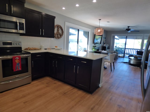 kitchen with light countertops, appliances with stainless steel finishes, open floor plan, light wood-type flooring, and a peninsula