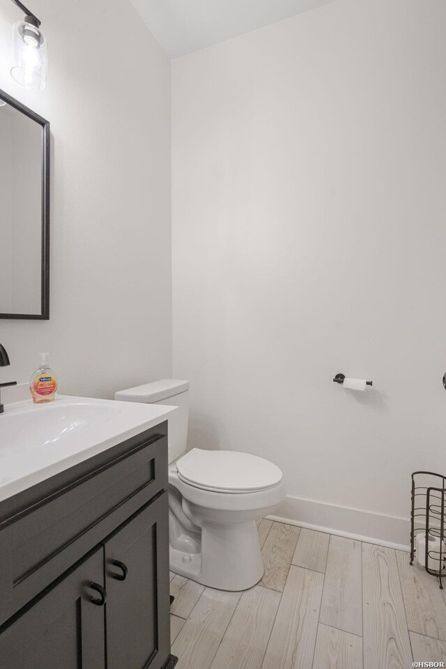 bathroom with baseboards, vanity, toilet, and wood finished floors