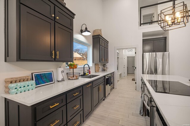 kitchen featuring a sink, a towering ceiling, appliances with stainless steel finishes, light wood finished floors, and decorative light fixtures