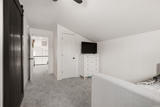 unfurnished bedroom with lofted ceiling, light colored carpet, a barn door, ceiling fan, and baseboards