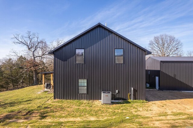 view of side of property featuring board and batten siding, an outbuilding, central AC, and a yard