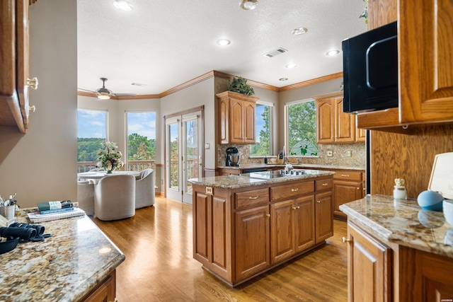 kitchen with black microwave, brown cabinetry, light stone countertops, and a center island