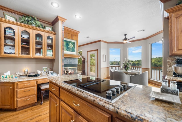 kitchen with built in desk, gas stovetop, visible vents, glass insert cabinets, and brown cabinetry