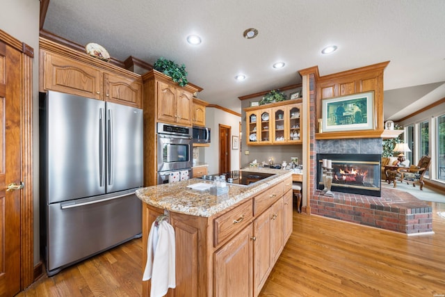 kitchen with a center island, light wood-style flooring, appliances with stainless steel finishes, glass insert cabinets, and light stone countertops