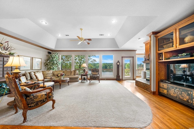 living area featuring visible vents, a raised ceiling, ceiling fan, light wood-style flooring, and a textured ceiling