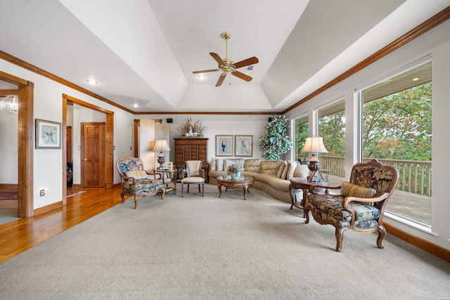 carpeted living room featuring ceiling fan, wood finished floors, baseboards, a tray ceiling, and crown molding