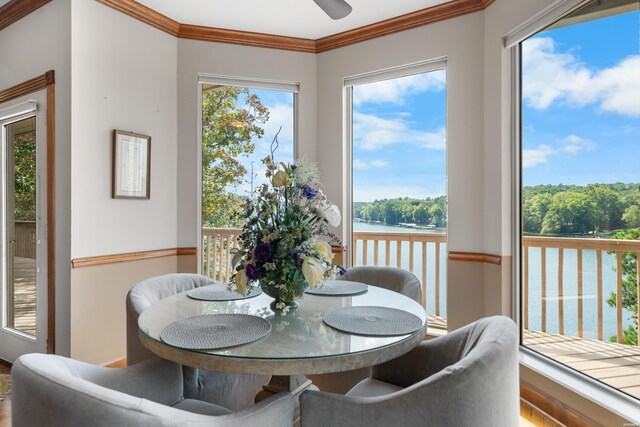 dining area featuring a ceiling fan, a water view, crown molding, and a view of trees