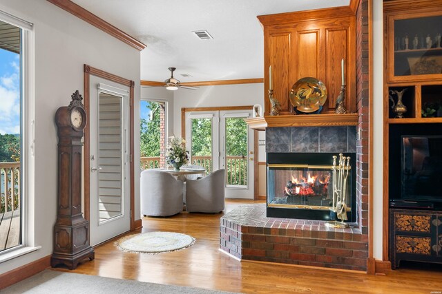 living area with visible vents, ceiling fan, ornamental molding, light wood-style floors, and a fireplace