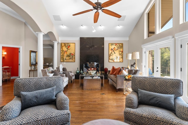 living area with a fireplace, decorative columns, a high ceiling, a ceiling fan, and wood finished floors