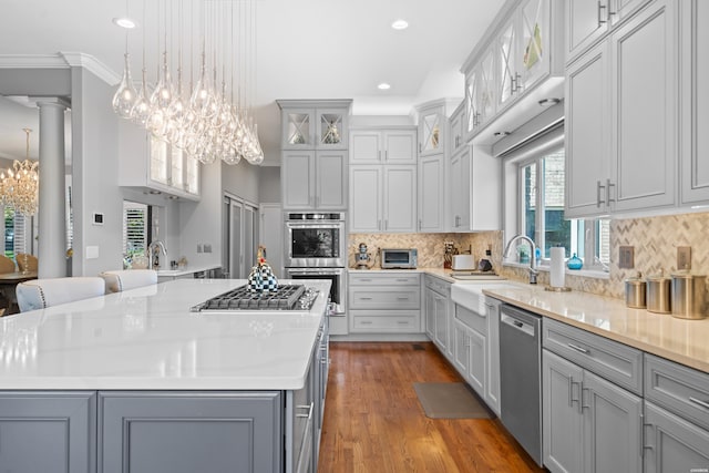 kitchen with stainless steel appliances, gray cabinets, a kitchen island, and glass insert cabinets