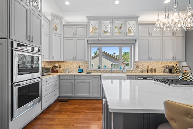 kitchen featuring glass insert cabinets, stainless steel double oven, light countertops, and a sink