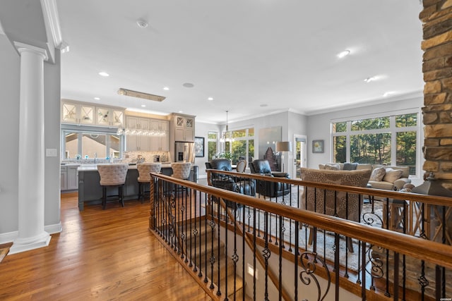 corridor with wood finished floors, ornamental molding, decorative columns, and an upstairs landing