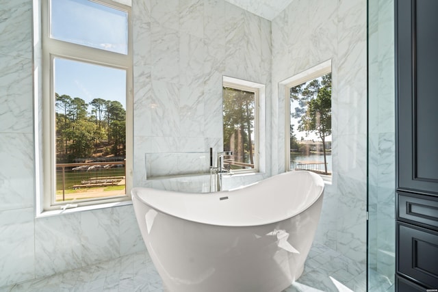 bathroom featuring a water view, a soaking tub, marble finish floor, and tile walls