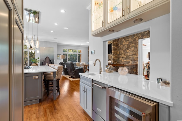 kitchen with wine cooler, a sink, open floor plan, light countertops, and gray cabinets