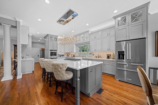 kitchen featuring a breakfast bar area, light countertops, appliances with stainless steel finishes, glass insert cabinets, and a kitchen island