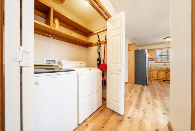 clothes washing area with light wood-type flooring, laundry area, a textured ceiling, and washer and dryer