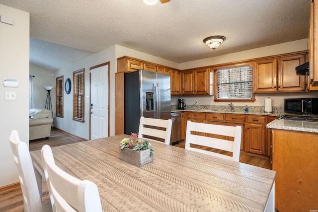 kitchen featuring brown cabinets, light wood-style flooring, appliances with stainless steel finishes, a sink, and ventilation hood