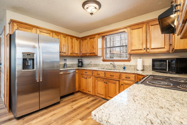 kitchen featuring light wood-type flooring, brown cabinets, stainless steel appliances, and a sink