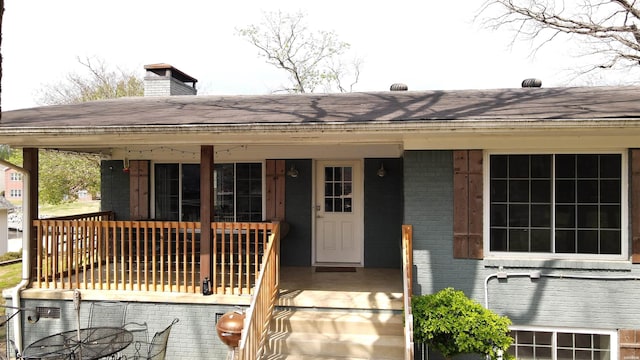 view of front of property with a shingled roof, brick siding, and a chimney