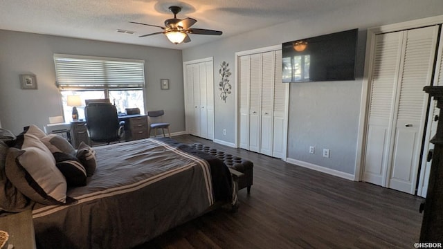 bedroom featuring a textured ceiling, dark wood-type flooring, visible vents, baseboards, and two closets