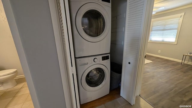 laundry room with tile patterned flooring, stacked washer and clothes dryer, baseboards, and laundry area