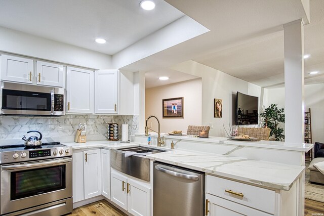 kitchen with appliances with stainless steel finishes, white cabinetry, a peninsula, and light stone countertops