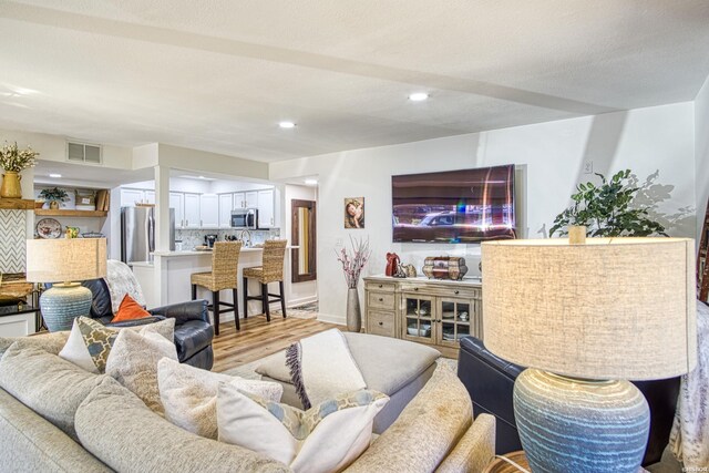 living area with a textured ceiling, light wood-style flooring, visible vents, and recessed lighting