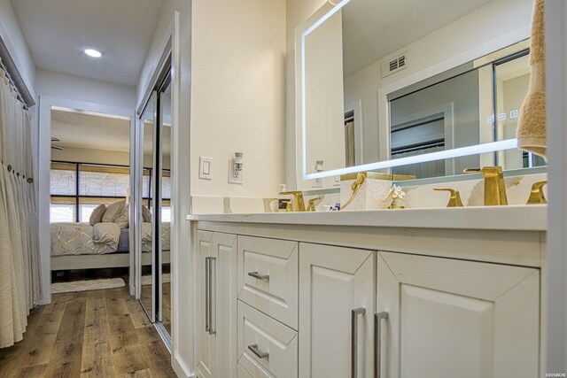 ensuite bathroom with double vanity, visible vents, connected bathroom, wood finished floors, and recessed lighting