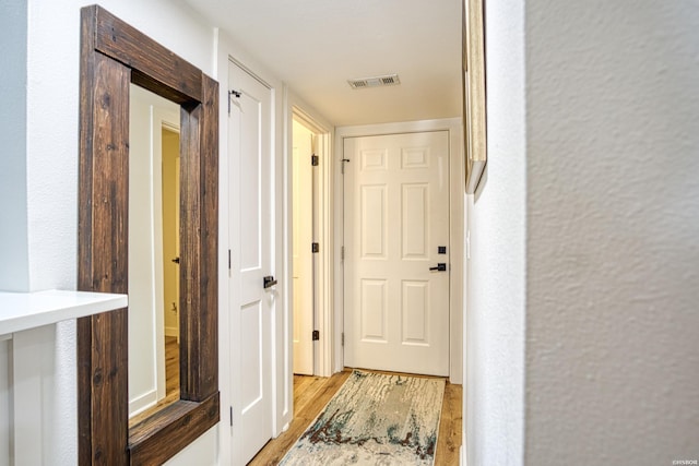 corridor with a textured wall, light wood-type flooring, and visible vents