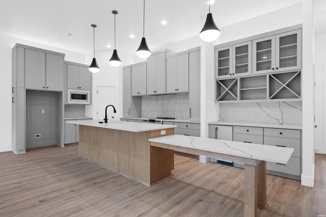 168 Krause Ln Unit B, Hot Springs, AR 71913 - kitchen with white microwave, gray cabinetry, light wood-style flooring, backsplash, and an island with sink