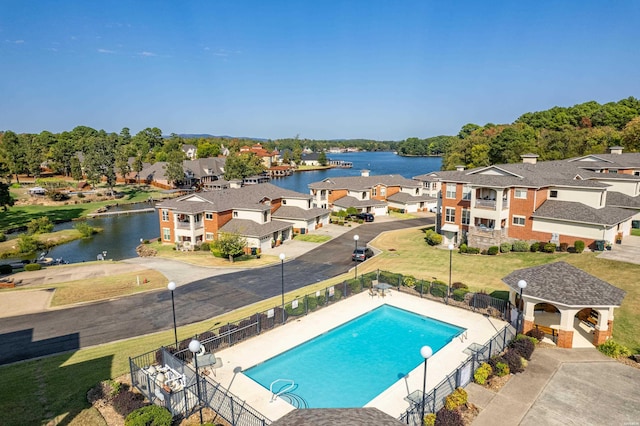 community pool with a water view, fence, and a residential view