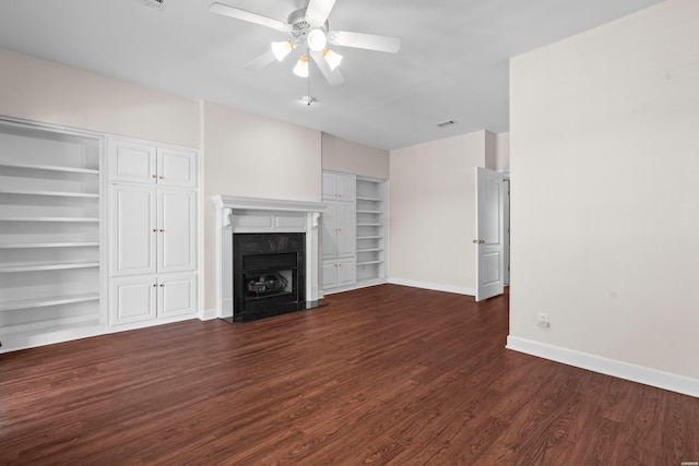 unfurnished living room featuring baseboards, dark wood finished floors, ceiling fan, built in shelves, and a fireplace