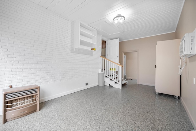 empty room featuring attic access, baseboards, brick wall, stairs, and speckled floor