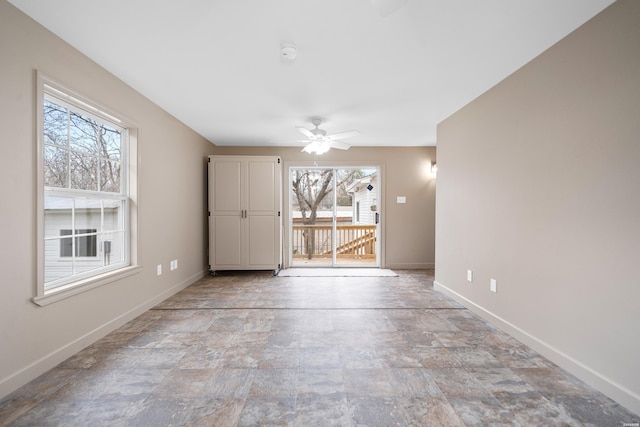 empty room with a ceiling fan, stone finish floor, and baseboards