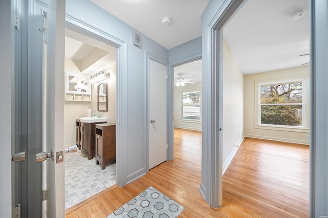 hall featuring visible vents, a sink, light wood-style flooring, and baseboards