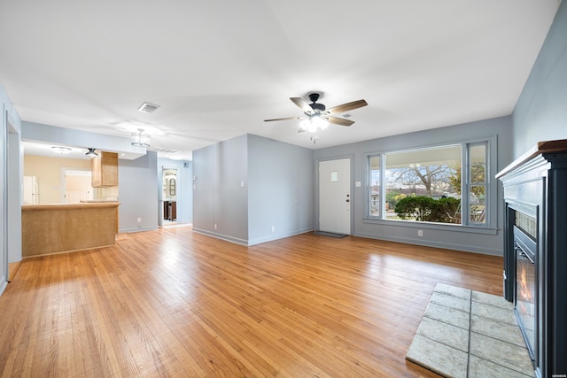 unfurnished living room with visible vents, baseboards, a glass covered fireplace, light wood-style flooring, and ceiling fan