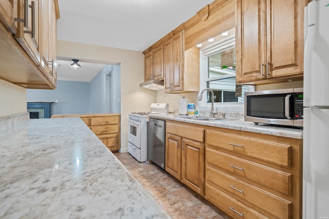 kitchen featuring light stone counters, under cabinet range hood, a fireplace, a sink, and appliances with stainless steel finishes