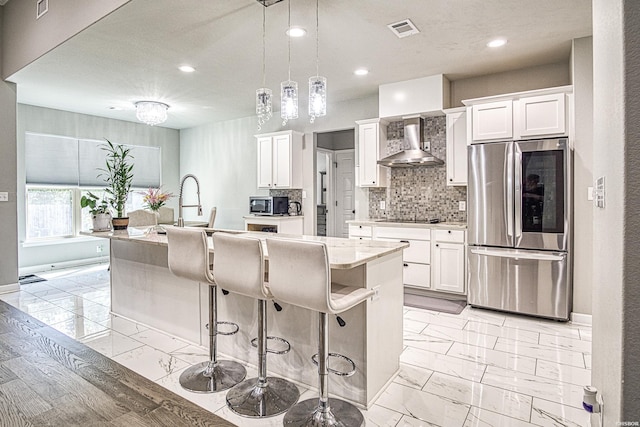 kitchen with marble finish floor, a center island with sink, stainless steel appliances, white cabinets, and wall chimney range hood