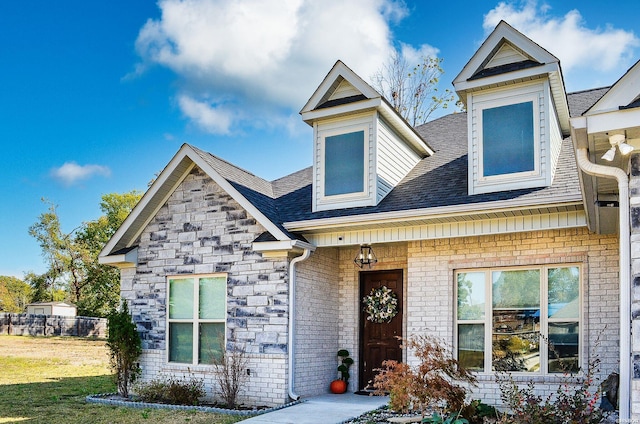 view of front of property featuring stone siding, brick siding, roof with shingles, and a front yard