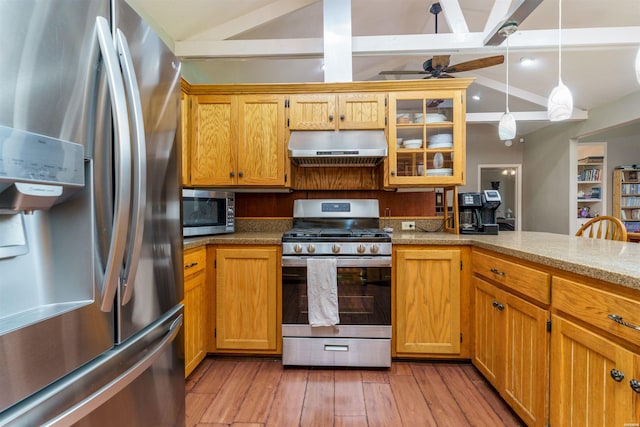 kitchen with glass insert cabinets, wall chimney range hood, light wood-style flooring, appliances with stainless steel finishes, and hanging light fixtures