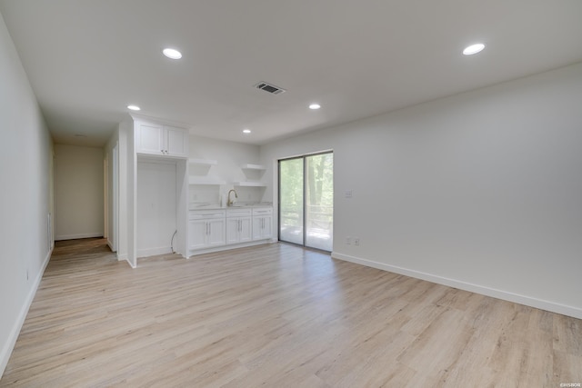 unfurnished living room with light wood-type flooring, visible vents, a sink, and recessed lighting