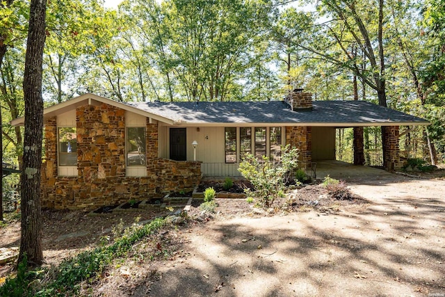 view of front of home with a carport, stone siding, driveway, and a chimney