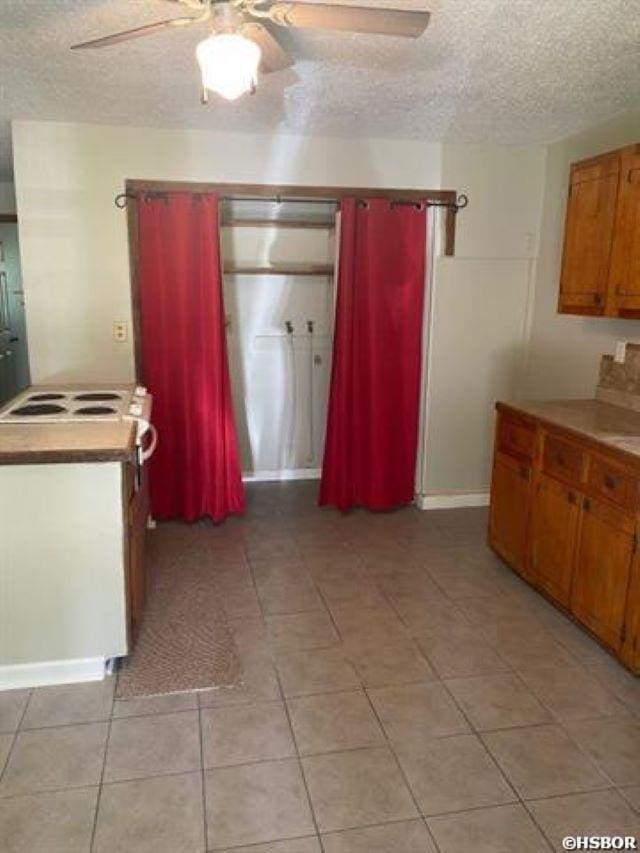 kitchen with a textured ceiling, light tile patterned flooring, brown cabinets, and ceiling fan