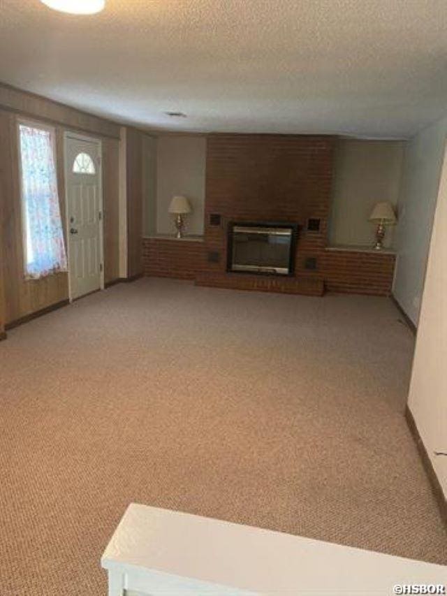 unfurnished living room featuring light colored carpet, a brick fireplace, and a textured ceiling